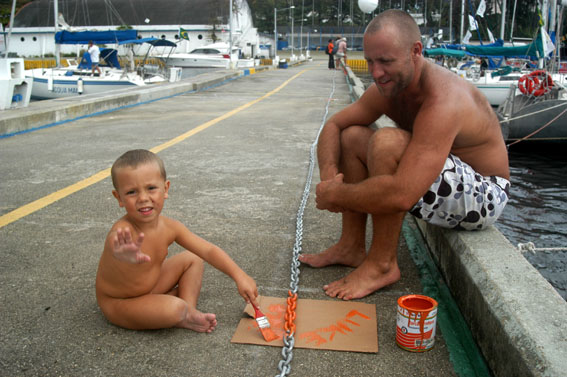 03RJ02.jpg - Todos trabalham na preparao dos barcos. Luke ajuda  o pai Ben a pintar a corrente do America